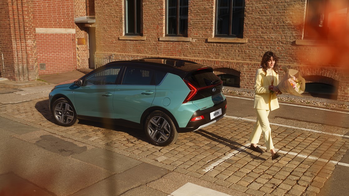 Kvinna med blombukett lämnar en grön Hyundai BAYON.